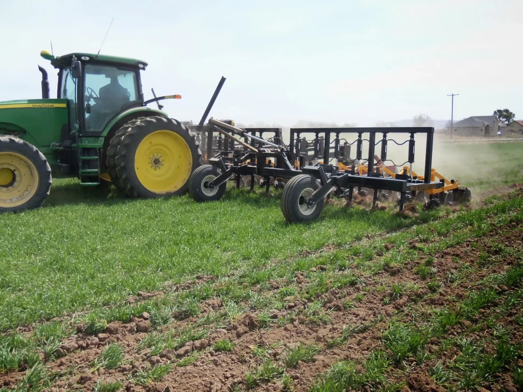 Strip-till bar behind a green tractor in a green field